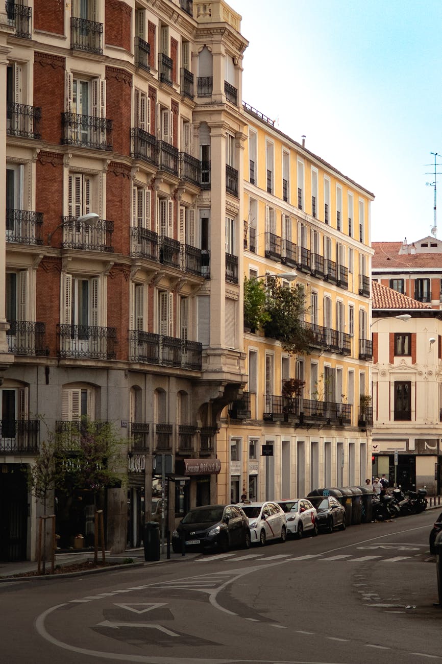 Madrid Chamberí neighborhood street at golden hour, warm European sandstone facades with terracotta balconies, soft evening foot traffic, editorial European street photography style, warm color grade anchored in cream and amber tones with subtle red accents from awnings and signage
