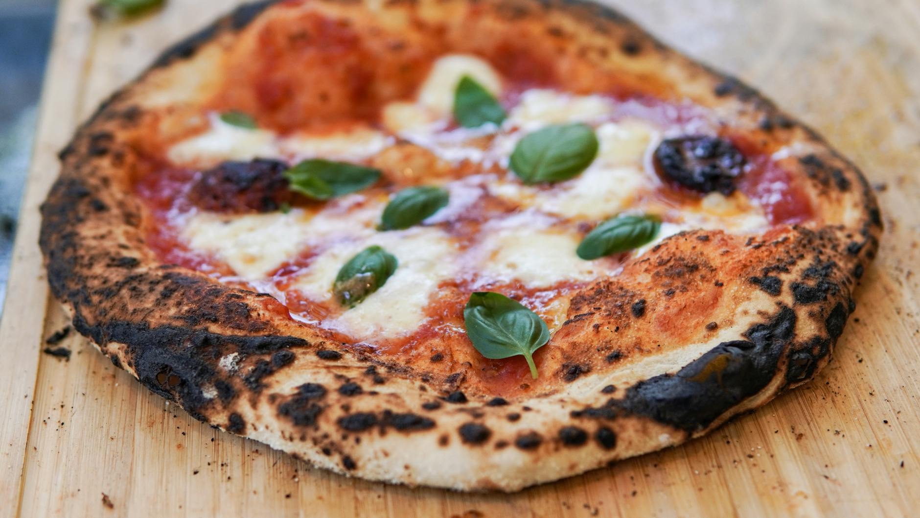 Fresh artisan margherita pizza with charred crust bubbles and melted mozzarella on wooden board