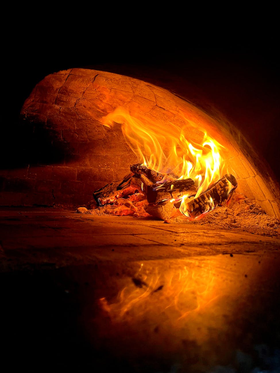 Wood-fired stone pizza oven interior with glowing flames visible inside brick chamber